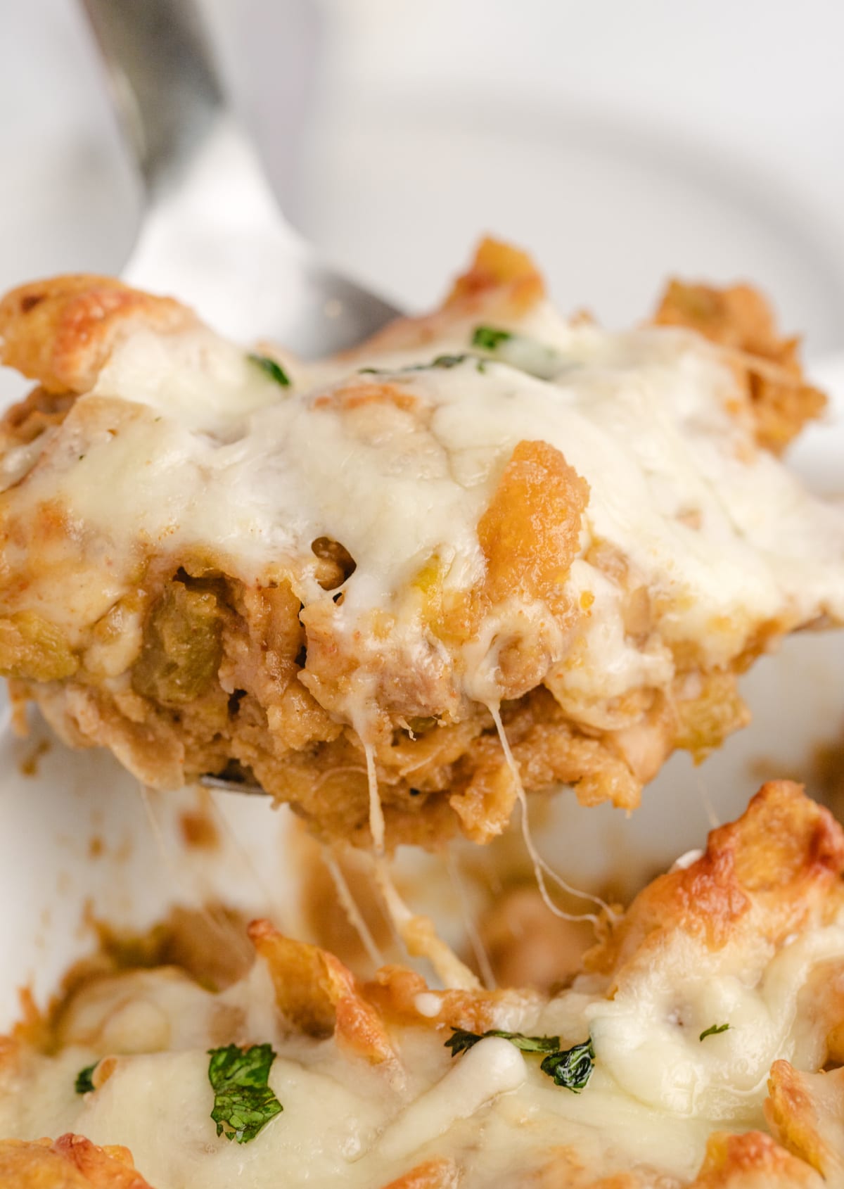 Spoon lifting a serving of Chicken Frito Pie Casserole from the dish, showing texture and melted cheese.