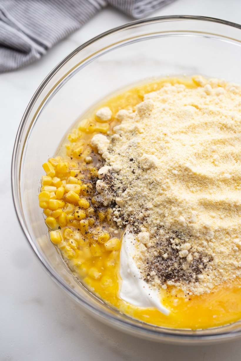 Overhead view of a mixing bowl filled with corn pudding ingredients before being stirred together.