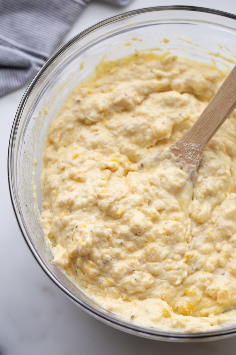 Corn pudding batter fully combined in a mixing bowl, with a wooden spoon resting inside.