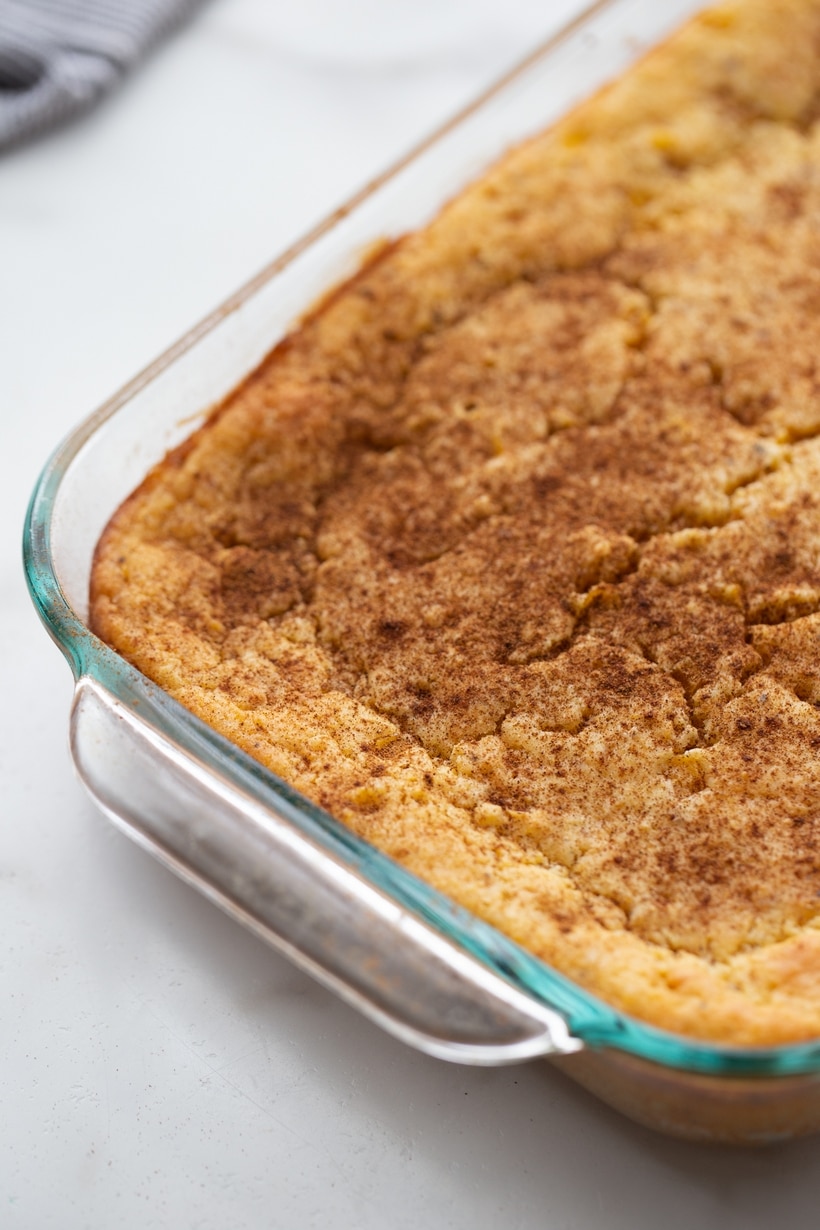 Corn pudding in a casserole dish after baking, lightly sprinkled with ground cinnamon on top.