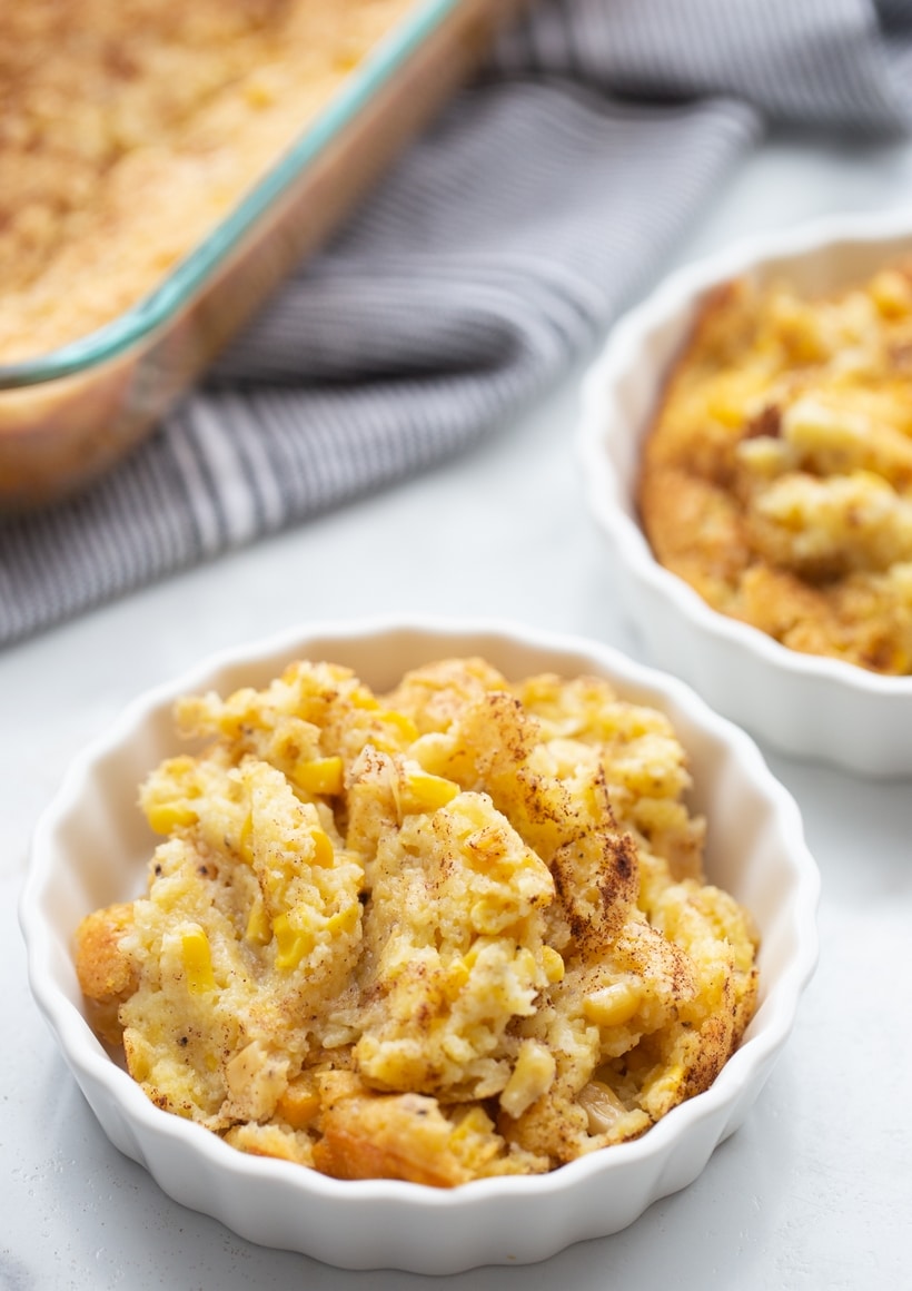 Individual serving of corn pudding in a white fluted ramekin, showing its golden, slightly textured top.