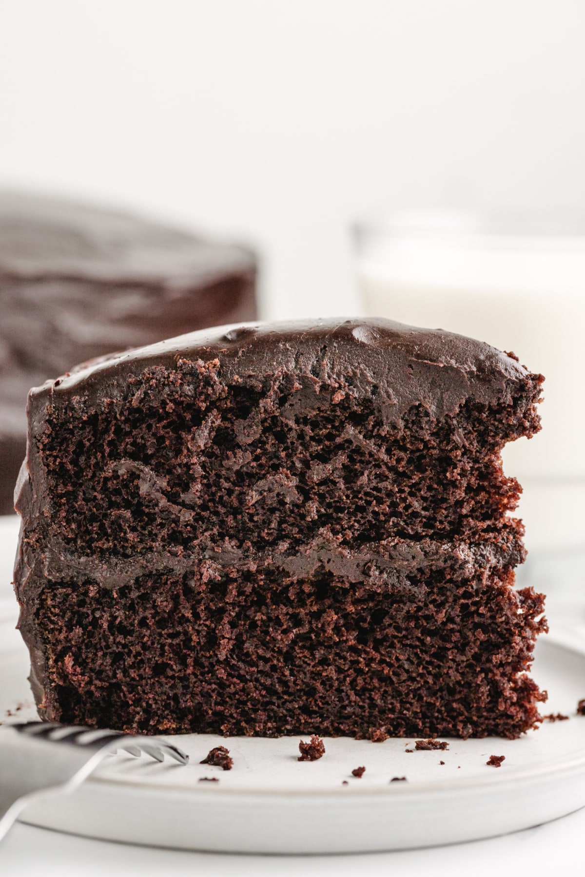 Close-up of a sliced piece of old-fashioned chocolate cake on a plate, showing its moist layers and glossy chocolate icing.