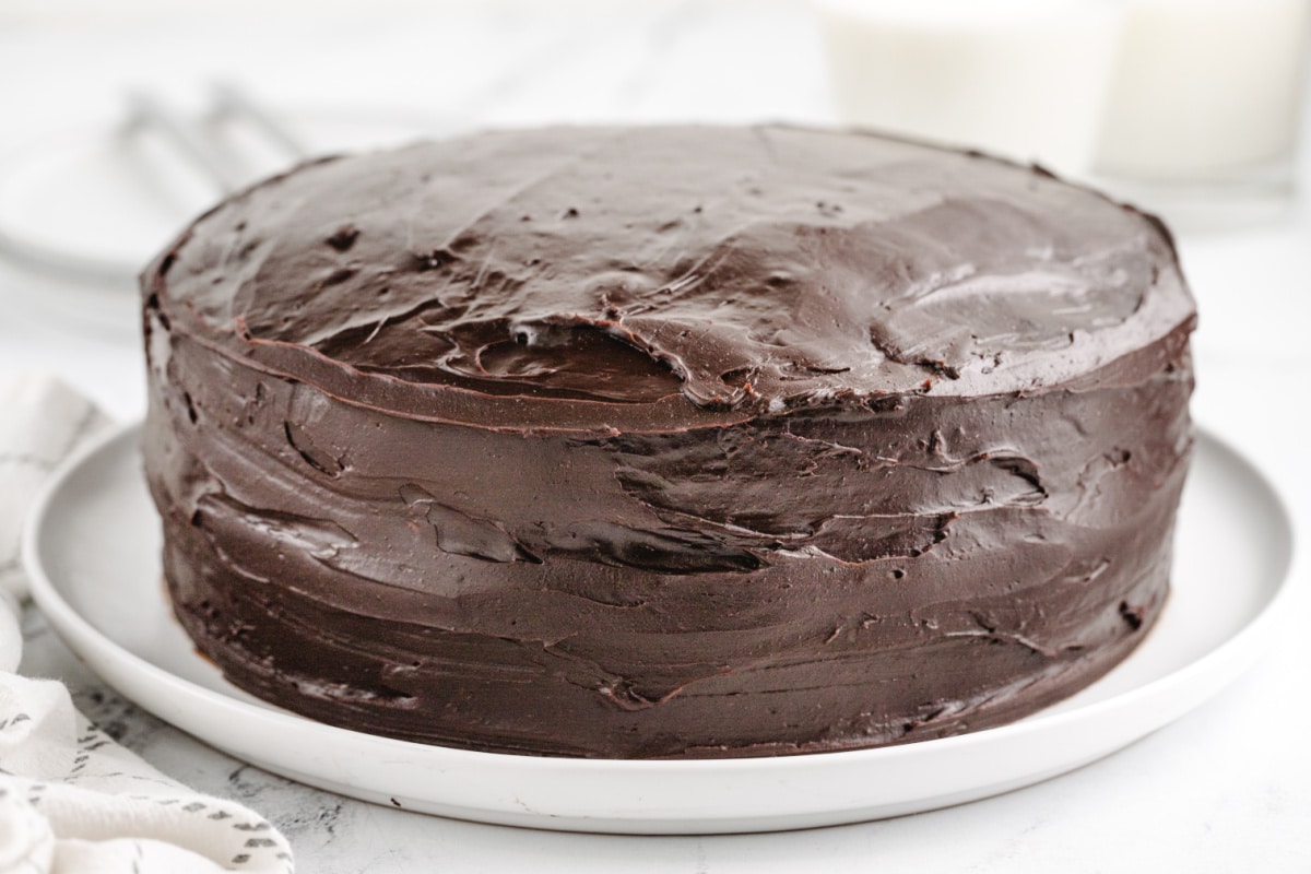 Whole old-fashioned chocolate cake on a cake stand, with thick chocolate icing covering the top and sides.