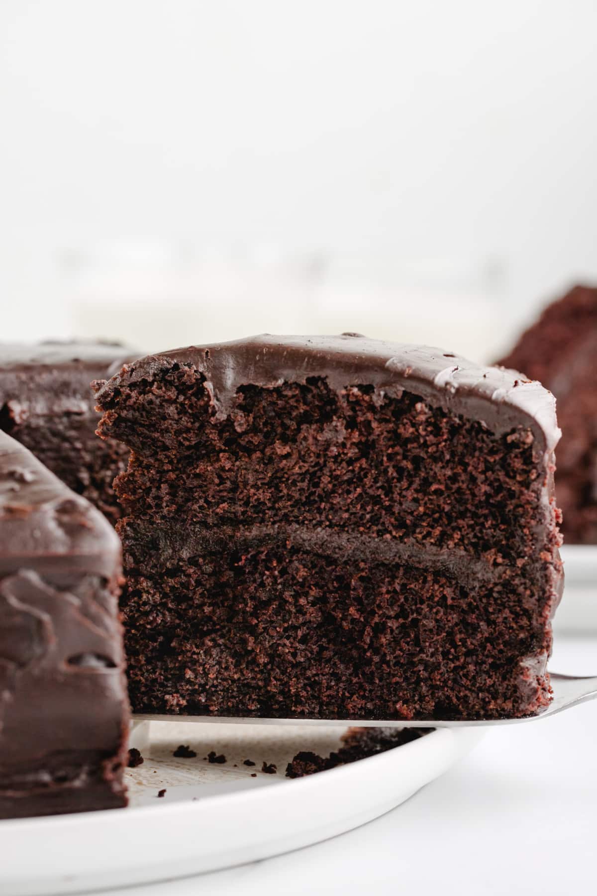 Side angle of a sliced piece of chocolate cake, with layers of glossy chocolate icing between soft cake layers.