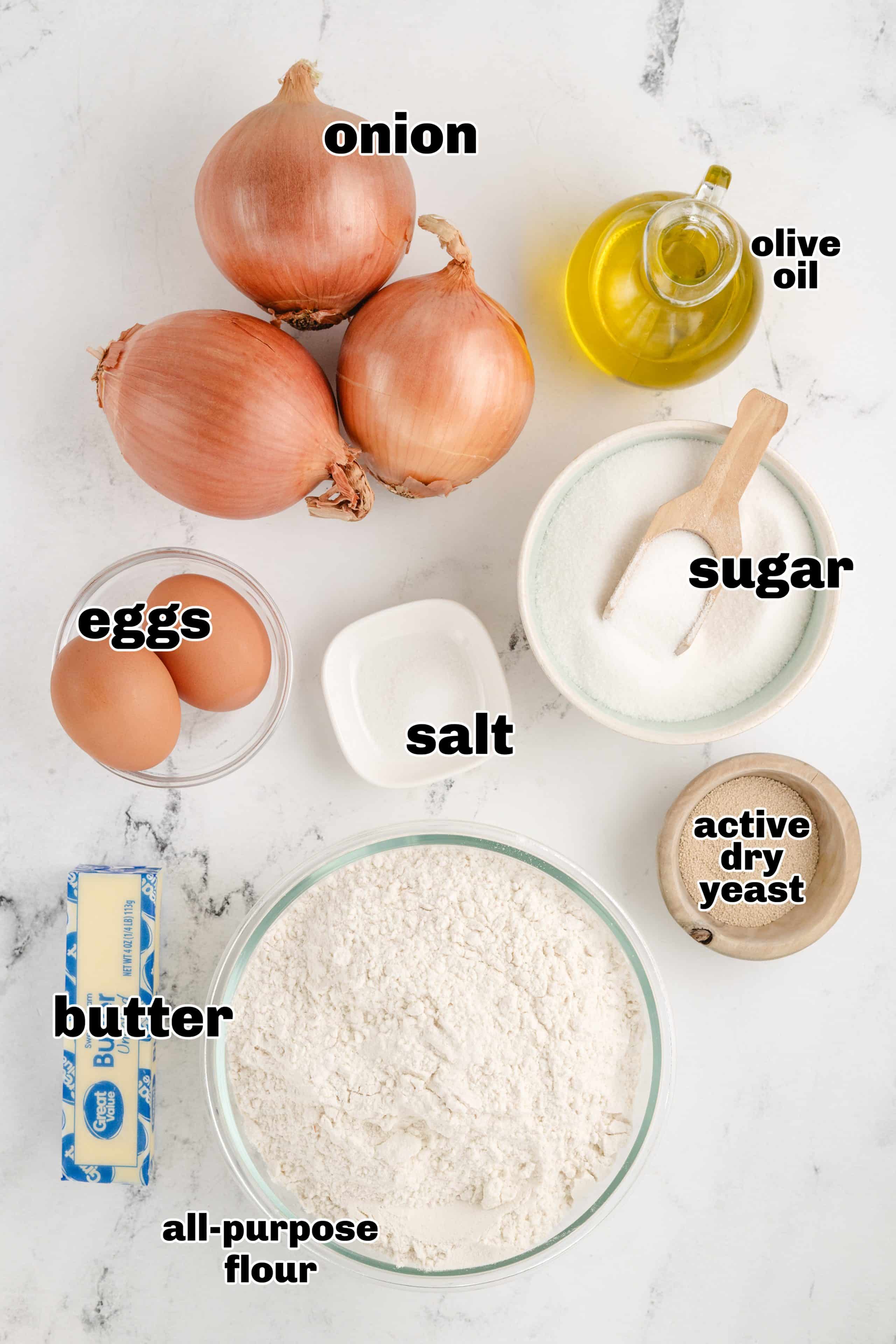 No-Knead Onion Rolls ingredients A display of ingredients for no-knead onion rolls, including flour, eggs, yeast, butter, and caramelized onions.