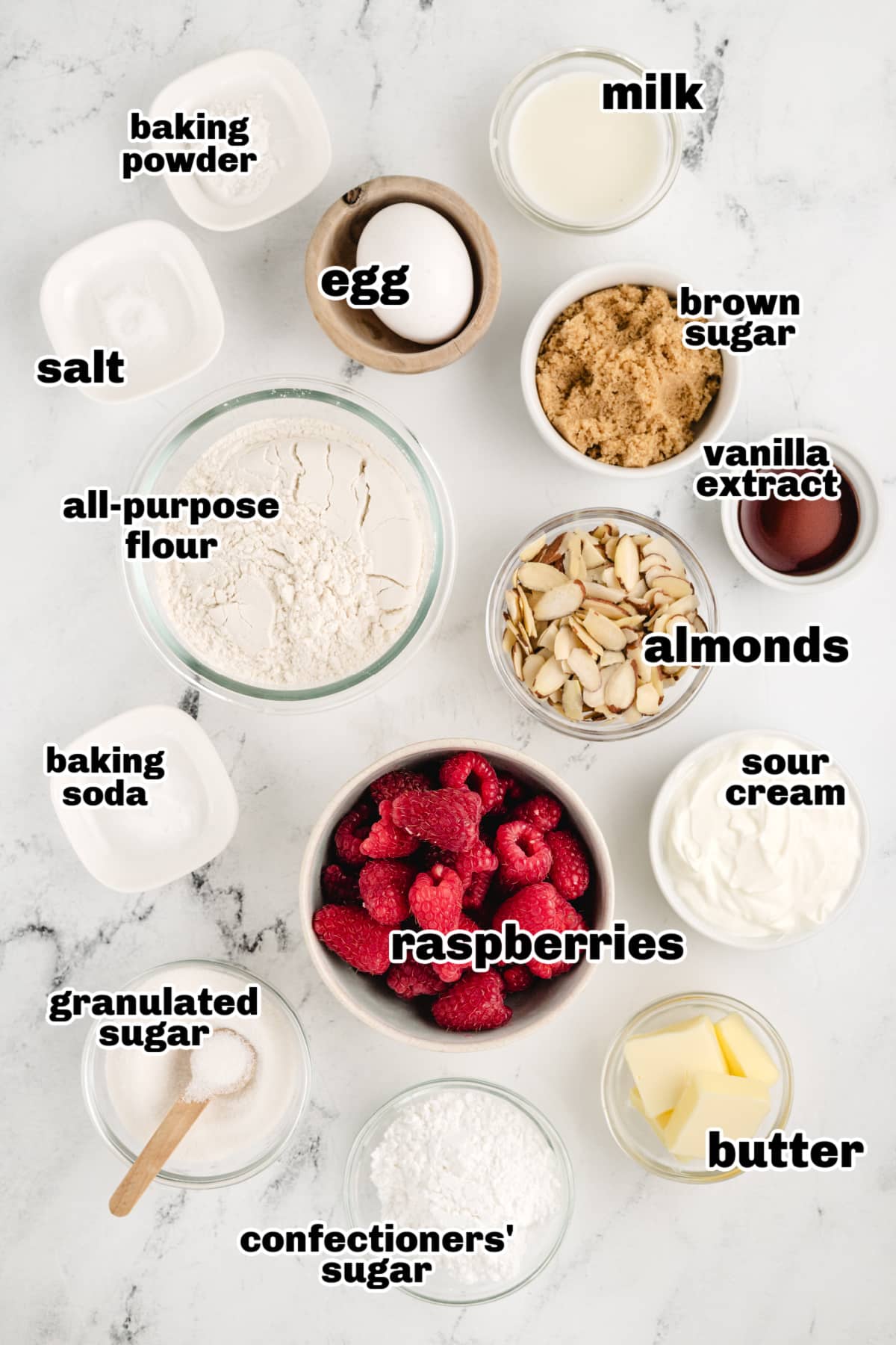 Overhead shot of all the ingredients for the raspberry almond coffee cake, including flour, sugar, eggs, butter, sour cream, raspberries, and almonds.