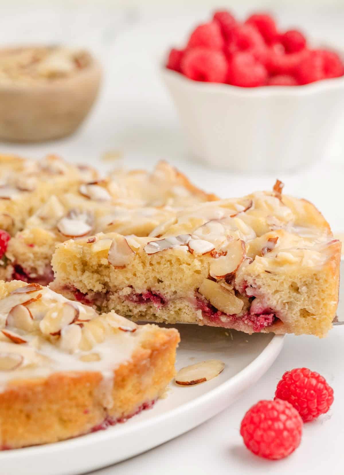 A single slice being lifted from the coffee cake, showing the soft texture, juicy raspberry filling, and crisp almond topping.