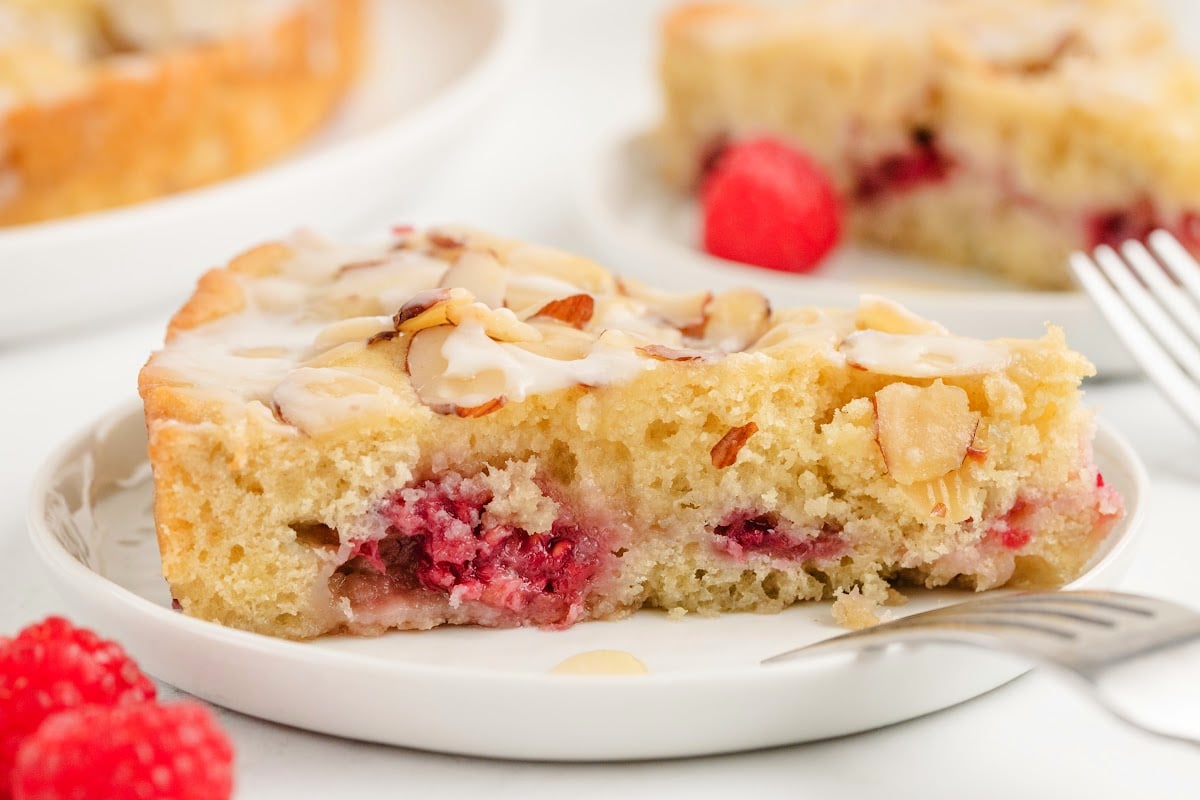 Side view of a full slice of raspberry almond coffee cake, highlighting the layers of tender cake, raspberries, and golden-brown almond topping.