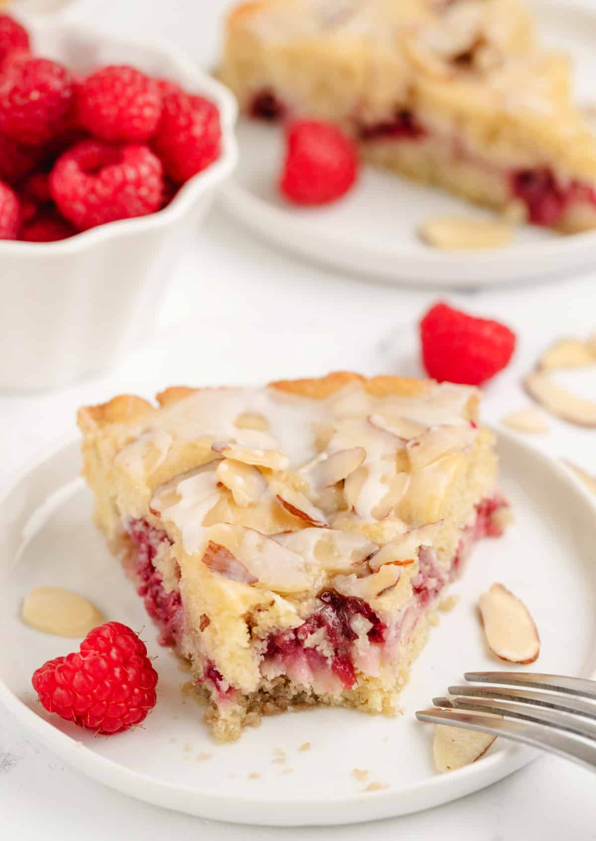 Close-up of a raspberry almond coffee cake slice with a bite removed, showing the soft crumb, juicy raspberries, and crunchy almond topping.