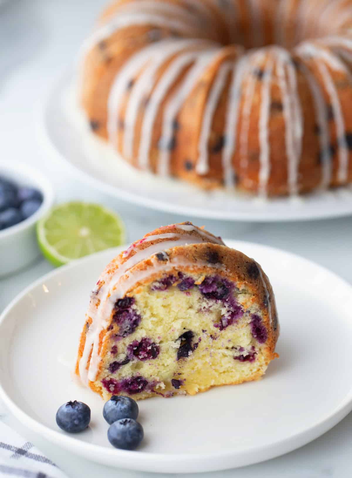 A close-up of a sliced piece of blueberry-lime pound cake with visible lime glaze and tender crumb.