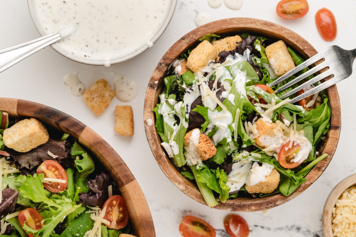 Mixed greens and croutons topped with creamy pesto salad dressing in a wooden bowl