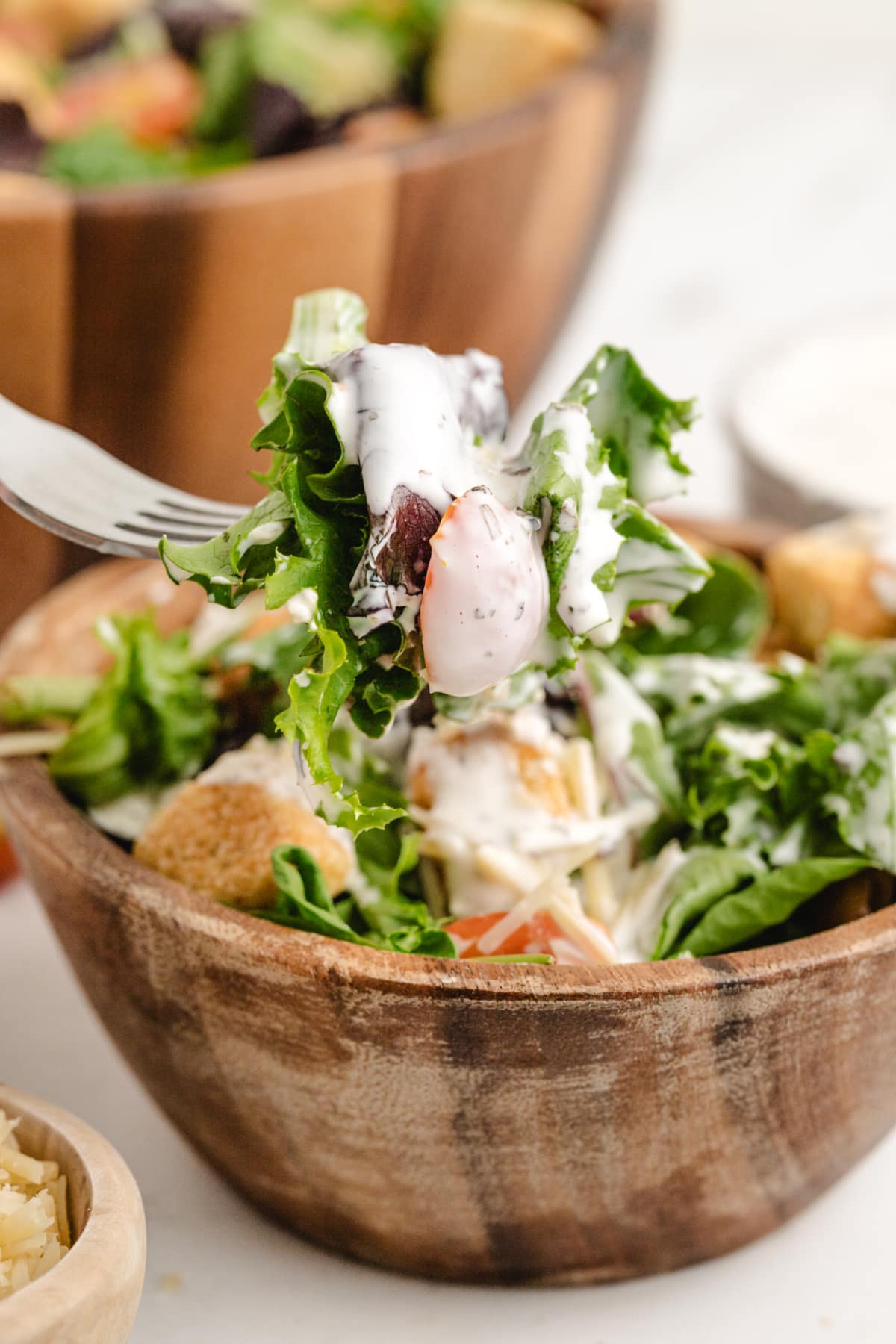 Fork lifting greens and tomatoes from a wooden bowl with creamy pesto dressing