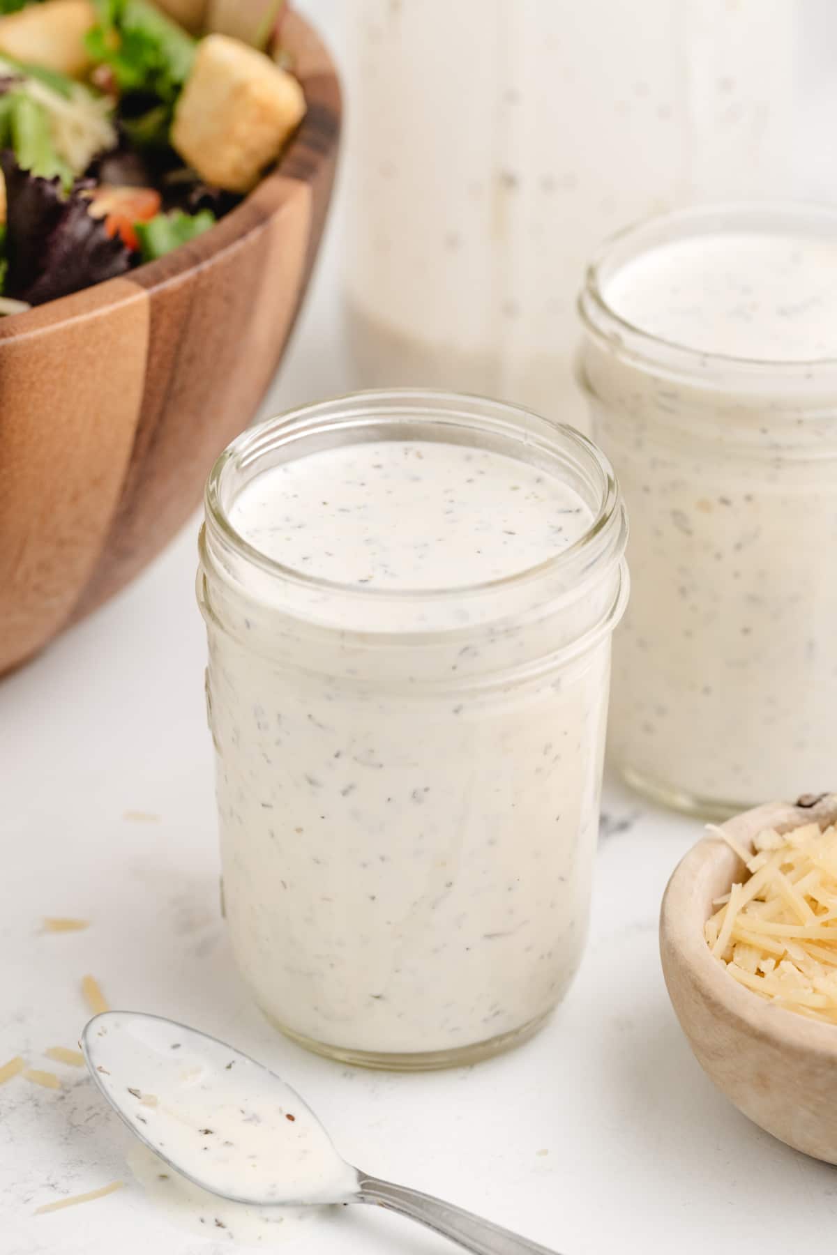 Mason jar filled with homemade creamy pesto dressing next to grated Parmesan and salad