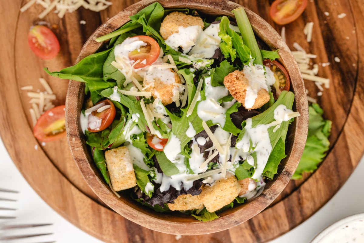 Overhead shot of salad drizzled with creamy pesto dressing and topped with croutons and cherry tomatoes