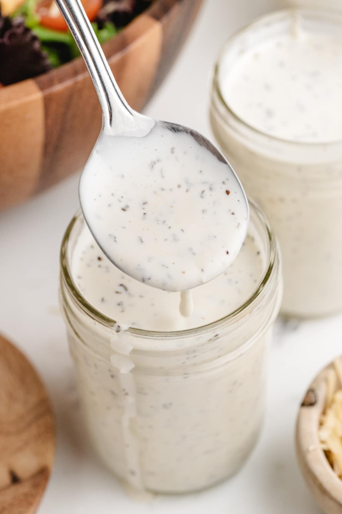 Spoonful of creamy pesto dressing dripping back into jar