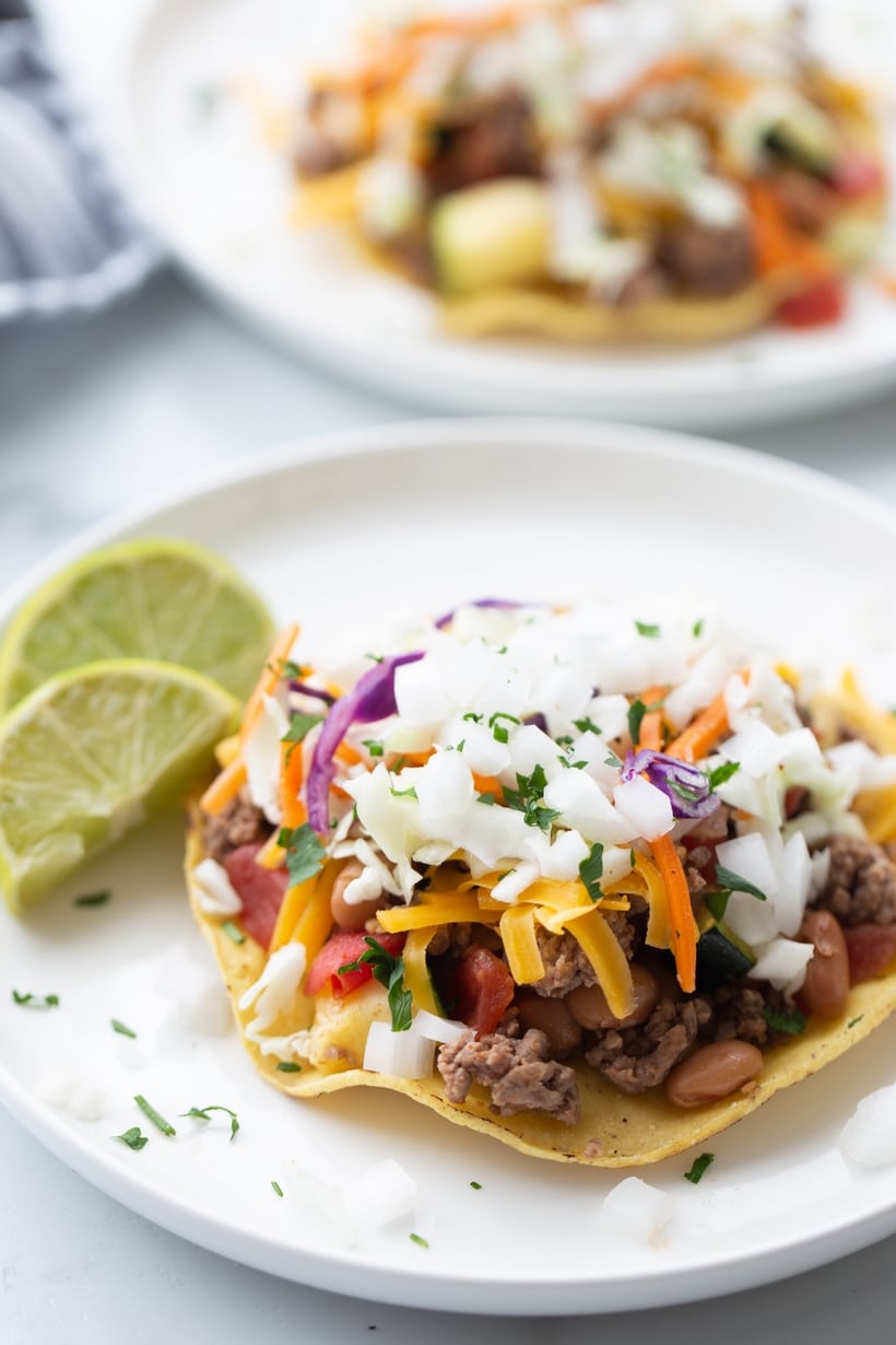 Finished Chipotle Beef Tostadas Ready to Serve Two finished chipotle beef tostadas with cheese, slaw, and lime wedges