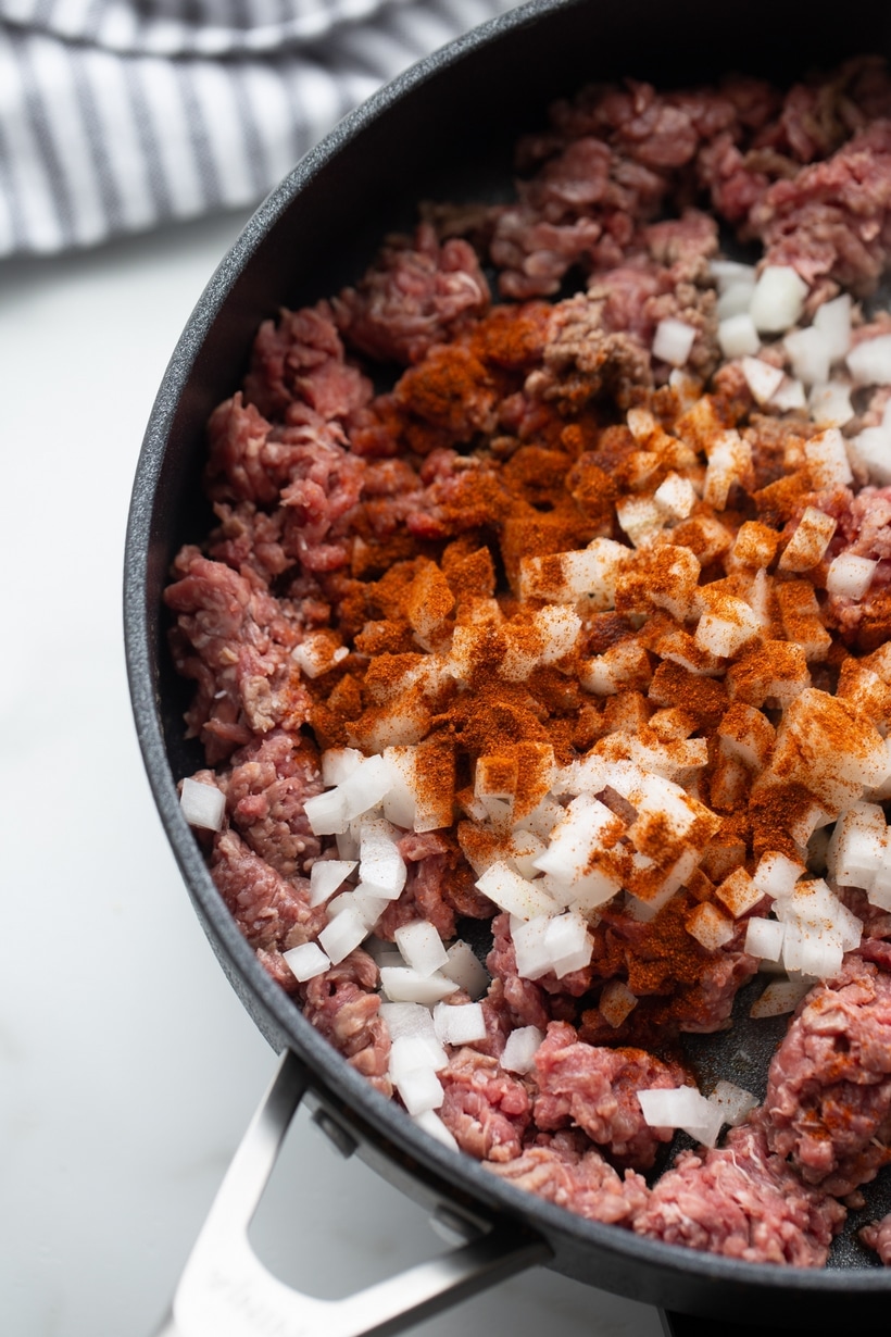 Ground Beef and Onion with Chipotle Seasoning Raw ground beef, chopped onion, and chipotle powder in skillet before cooking