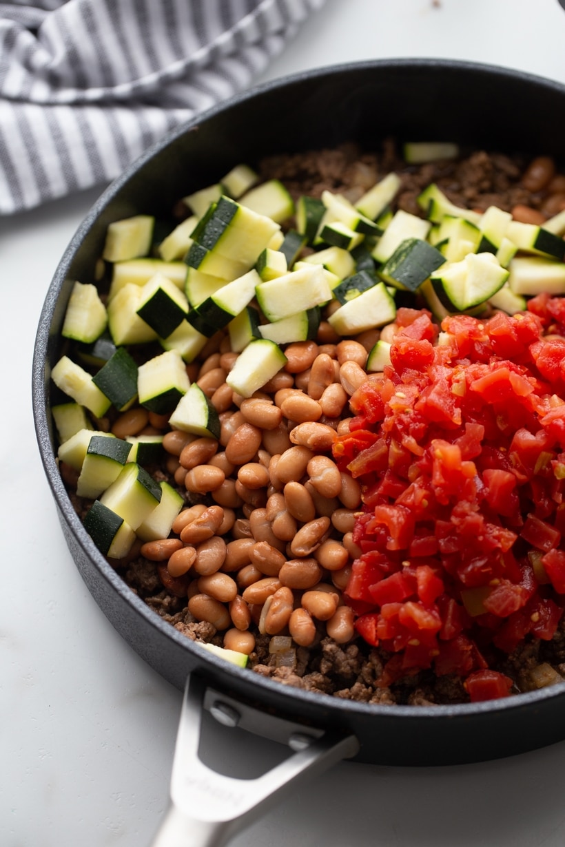Tex-Mex Beef Mixture Before Stirring Zucchini, fire-roasted tomatoes, and pinto beans on top of browned beef in skillet