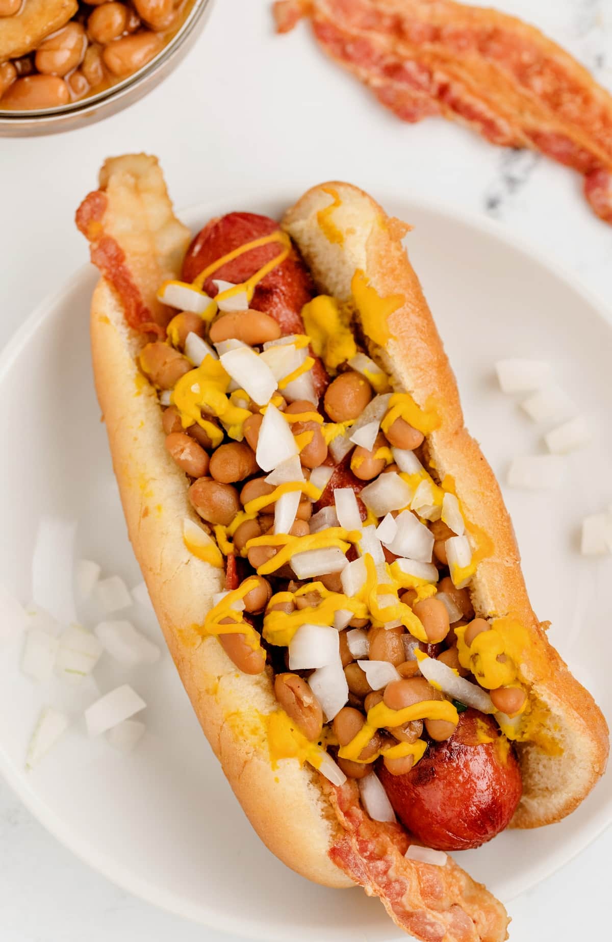Place cooked hot dogs in buns with a slice of bacon. Top with baked beans, white onion and yellow mustard. rustic ranch dog