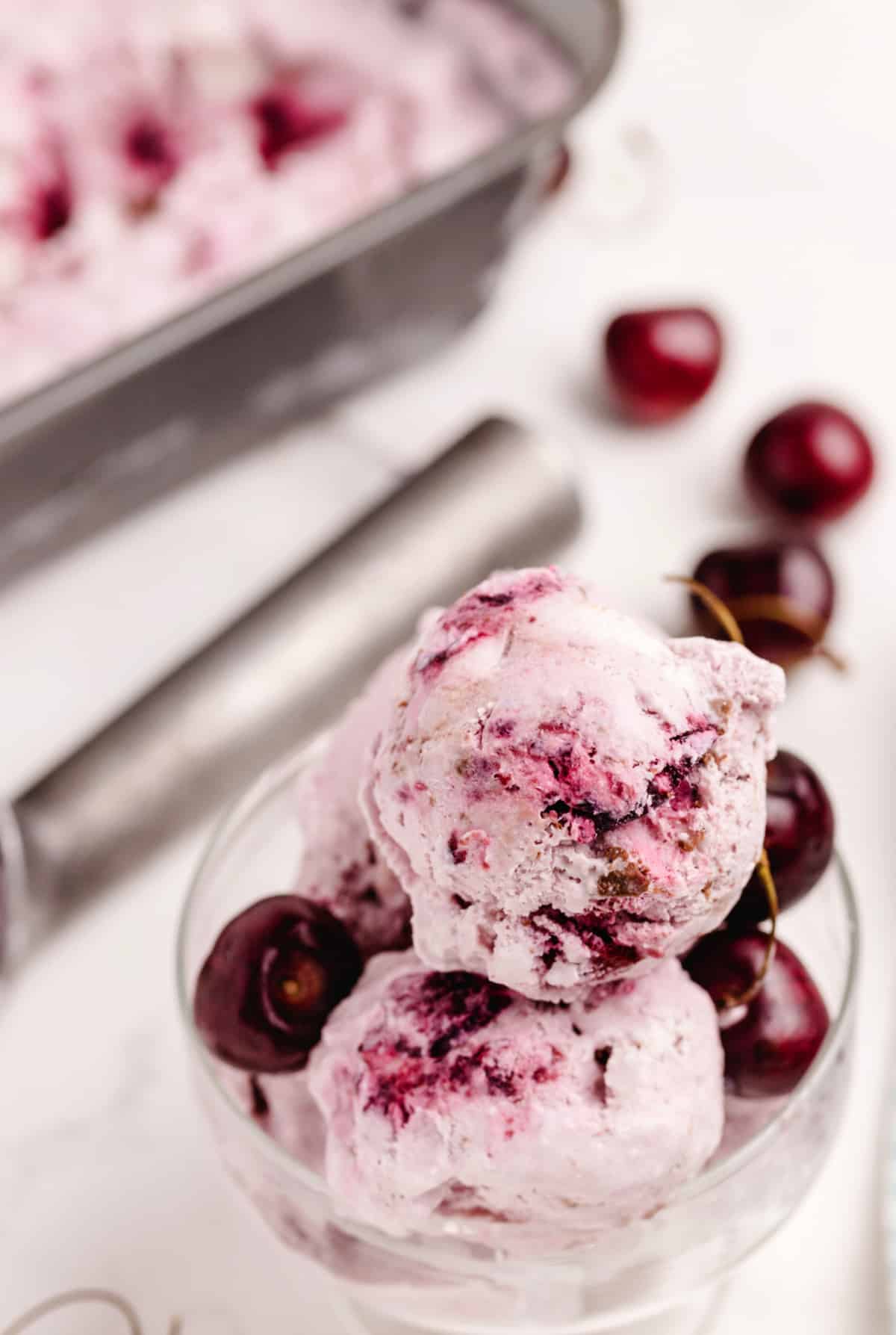 Fresh Cherry Coconut Chocolate Chip Ice Cream in Glass Scoops of fresh cherry coconut chocolate chip ice cream in a glass with whole cherries, highlighting creamy texture and real fruit.