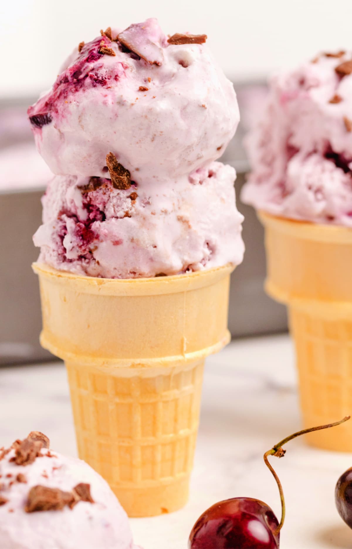 Cherry Coconut Chocolate Chip Ice Cream Cone Cherry coconut chocolate chip ice cream served in a cone with chopped chocolate pieces, showing churned texture and visible fruit swirls.