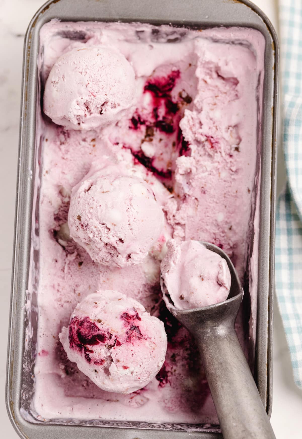 Scooped Fresh Cherry Coconut Chocolate Chip Ice Cream Container of churned fresh cherry coconut chocolate chip ice cream with a scoop and visible cherry swirls and chocolate chunks.