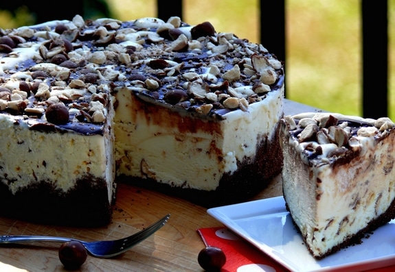 Whoppers Malted Milk Ice Cream Cake loaded with crushed malted milk balls, layered over a chocolate graham cracker crust, and topped with chocolate ganache. Whoppers Malted Milk Ice Cream Cake with a slice served alongside the cake, showing the malted milk ice cream filling, chocolate topping, and chocolate graham cracker crust.
