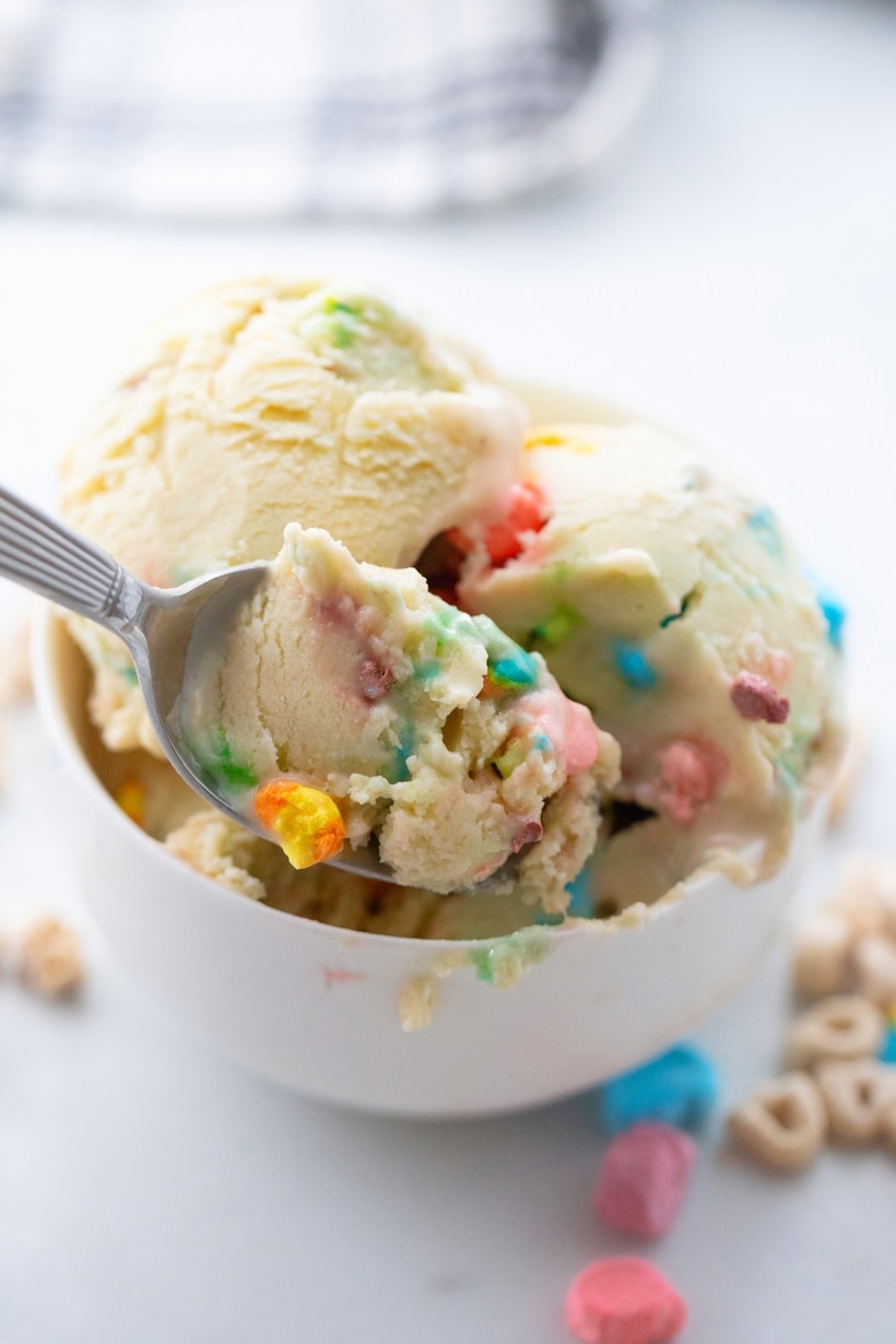 Lucky Charms Ice Cream spoonful A close-up of a spoon scooping creamy Lucky Charms Ice Cream from a bowl, showing the smooth texture and colorful marshmallows.
