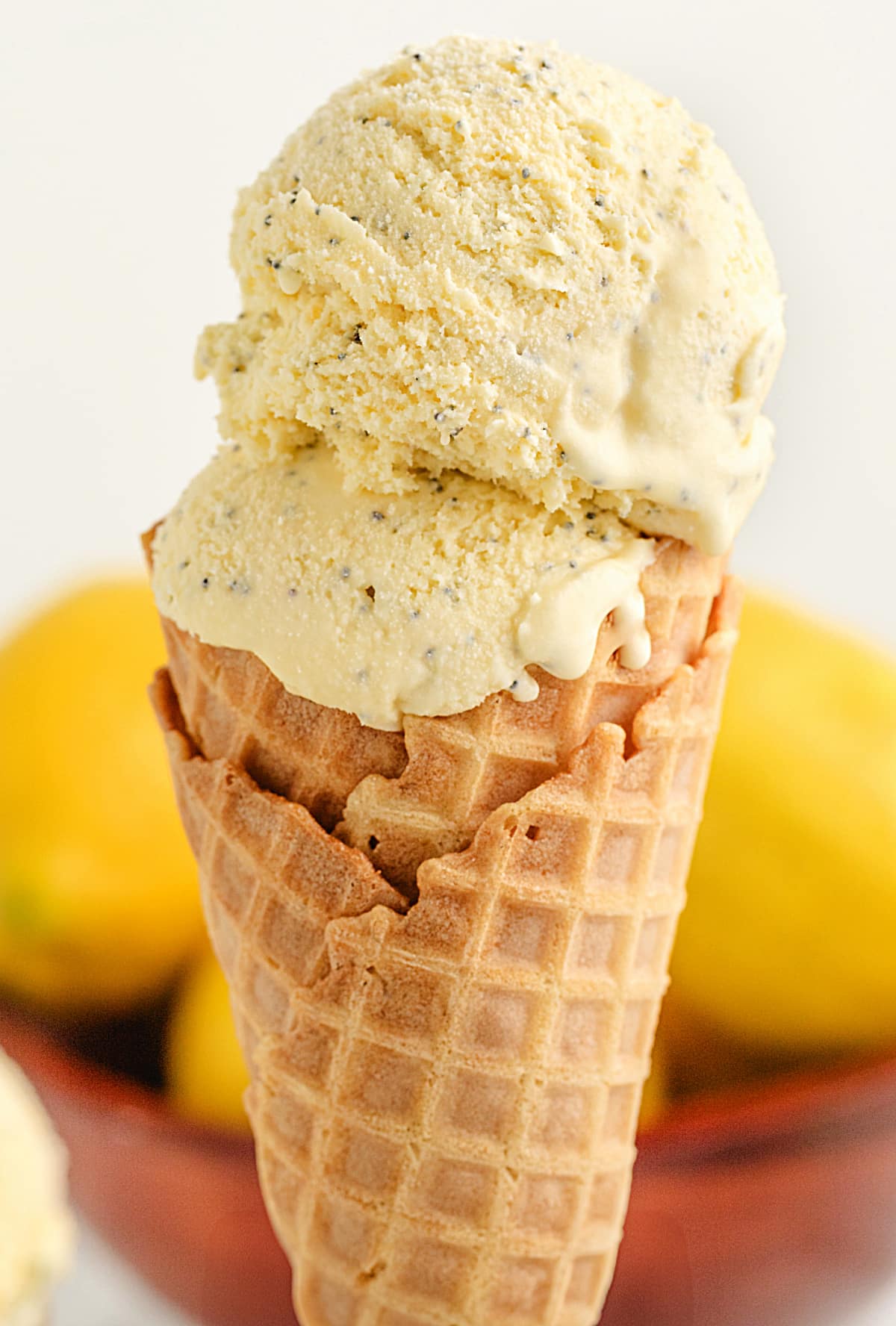 Lemon Poppy Seed Ice Cream Cone with Custard Base Double scoop of lemon poppy seed ice cream in a waffle cone with lemons in the background