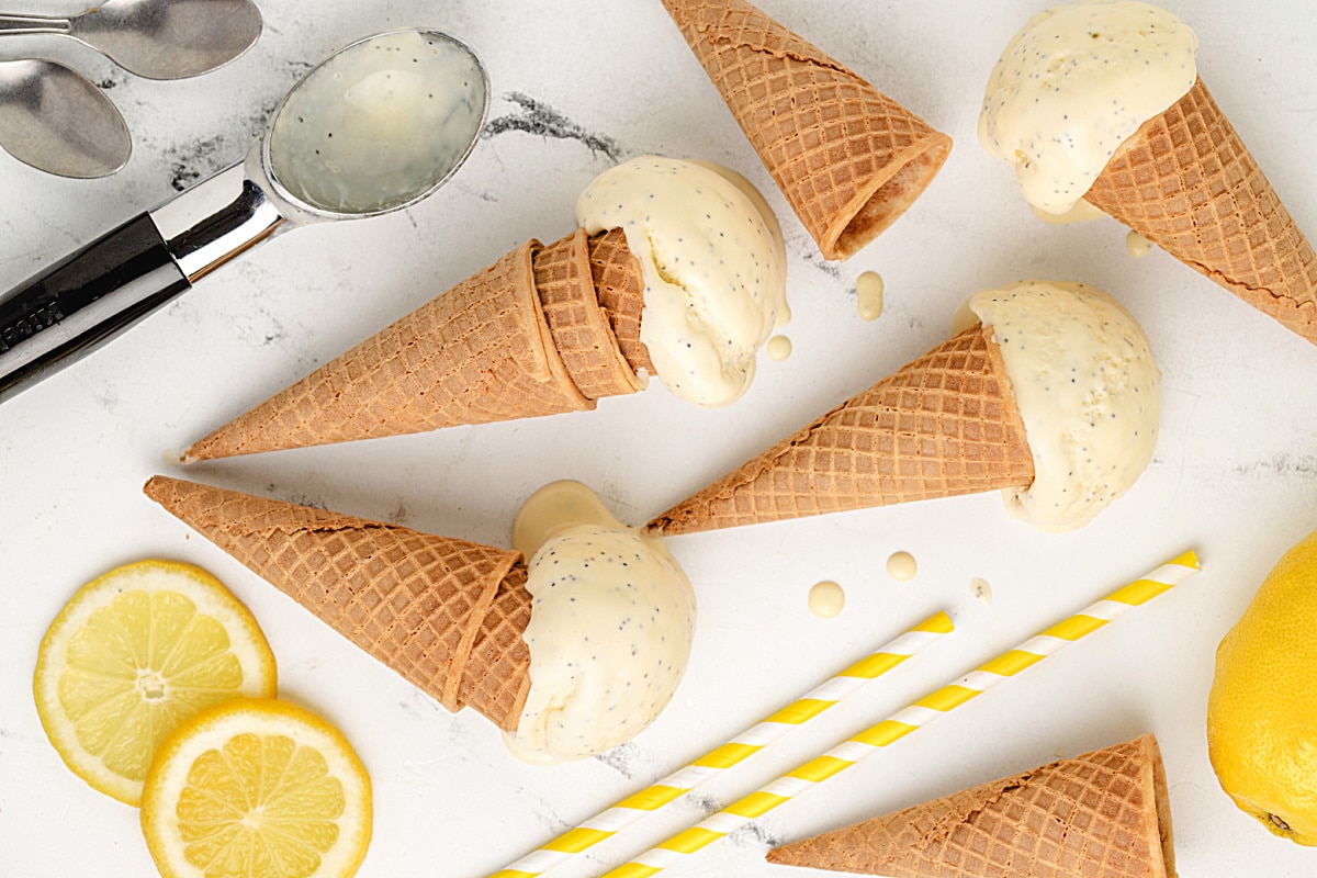 Soft-Set Lemon Poppy Seed Ice Cream in Waffle Cones Melted lemon poppy seed ice cream cones scattered on a white surface with lemon slices and spoons