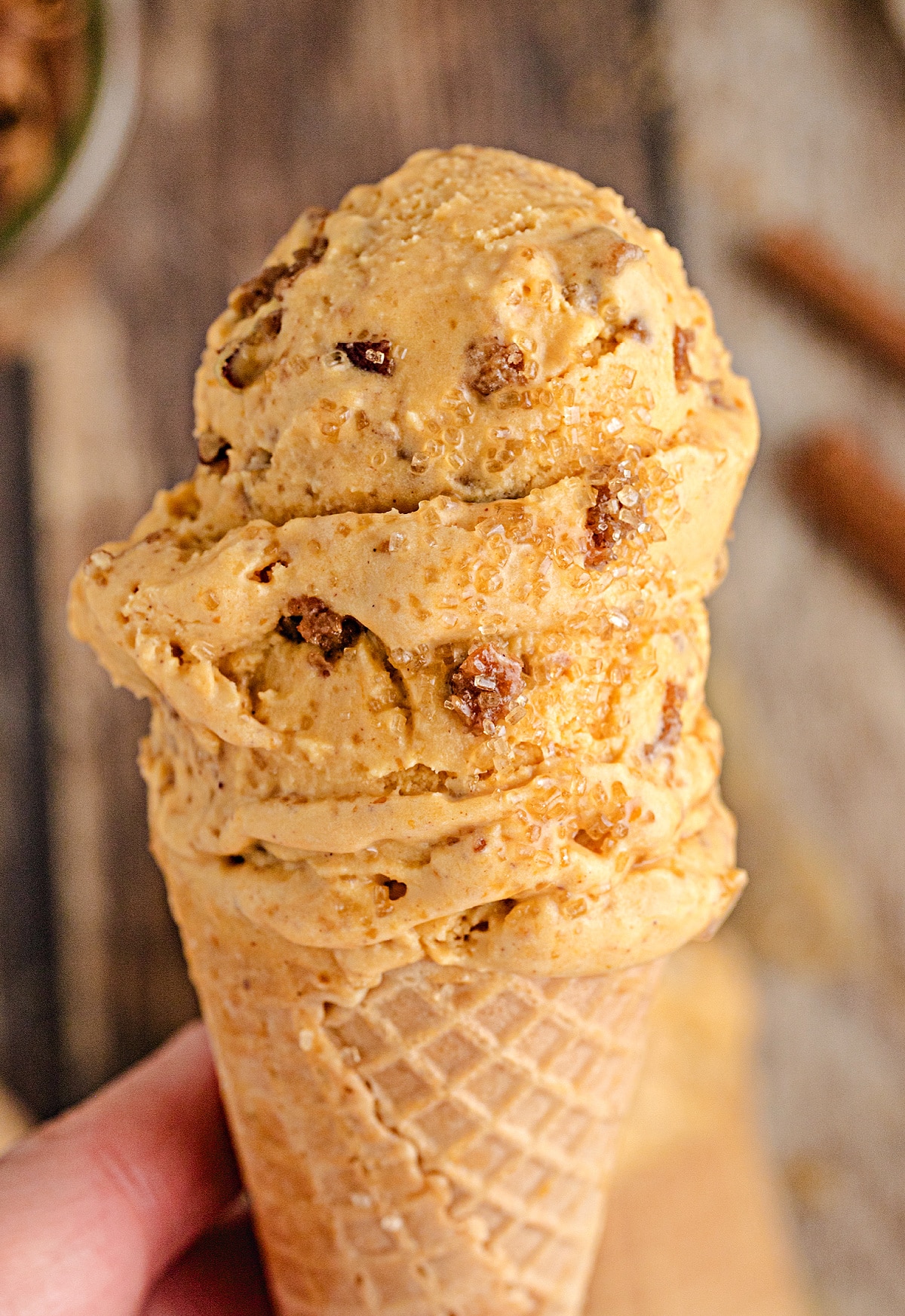 Pumpkin Brown Sugar Crunch Ice Cream in Waffle Cone Tall scoop of Pumpkin Brown Sugar Crunch Ice Cream in a waffle cone, showing creamy pumpkin custard texture with brown sugar streusel pieces and turbinado sparkle.