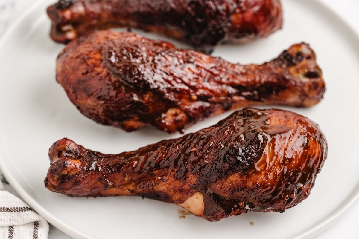 Three glazed chicken drumsticks served on a white plate