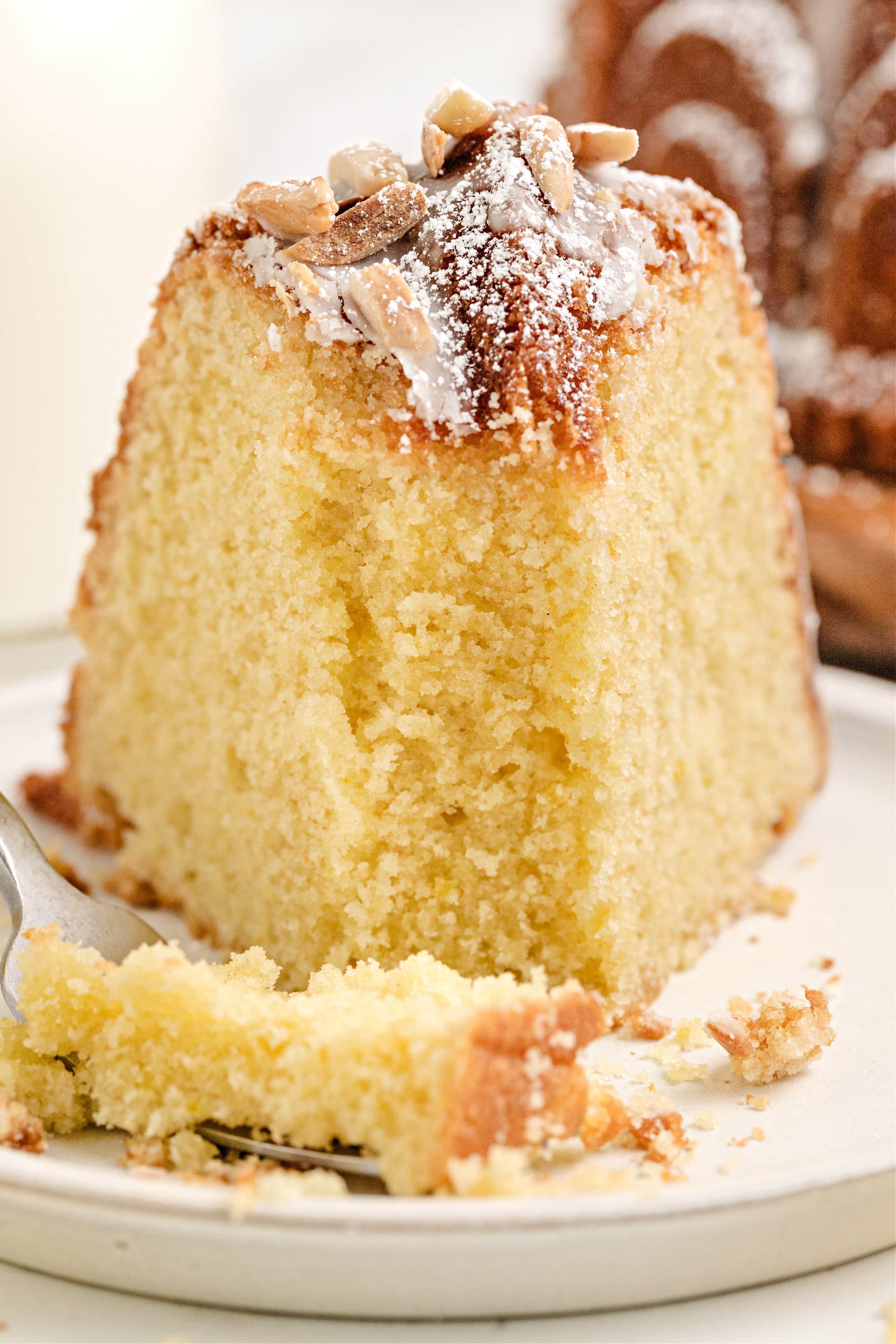 Plated Slice of Lemon Syrup Cake with Fork Single serving of lemon Bundt cake with toasted almond topping and soft texture