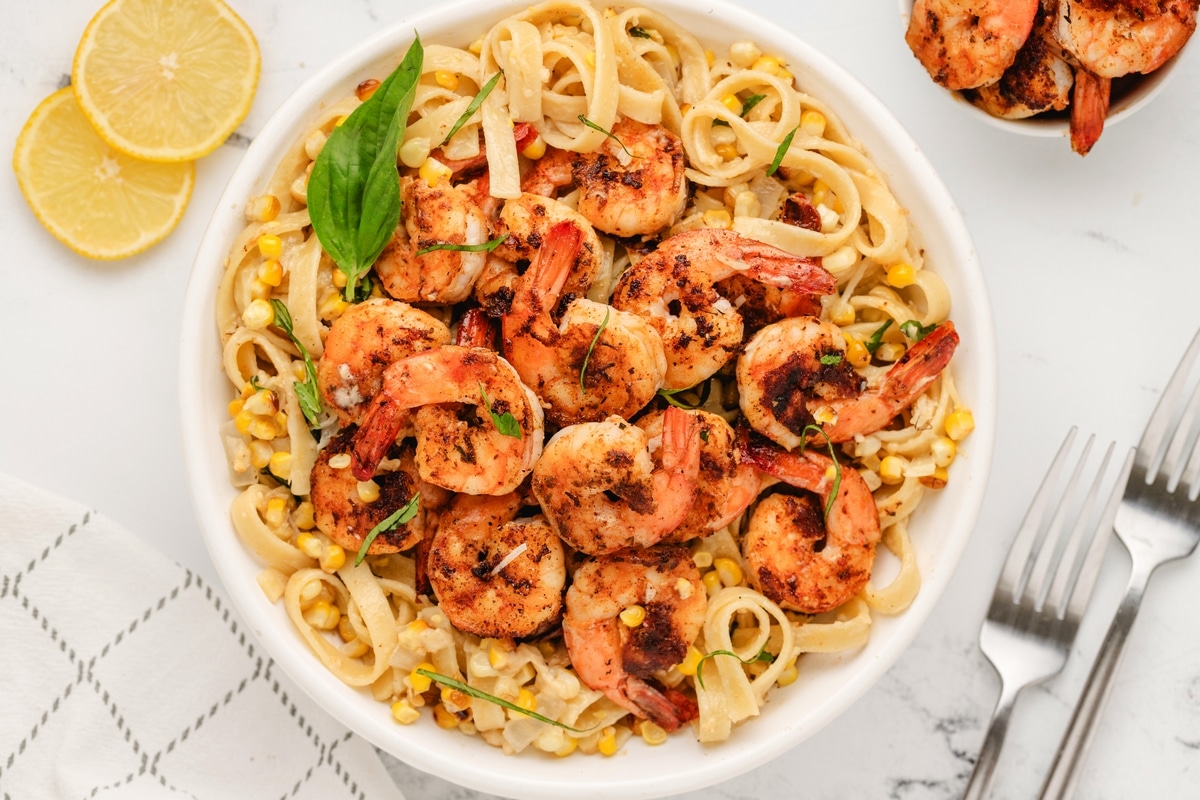 Family-style blackened shrimp pasta with corn and basil in white bowl.