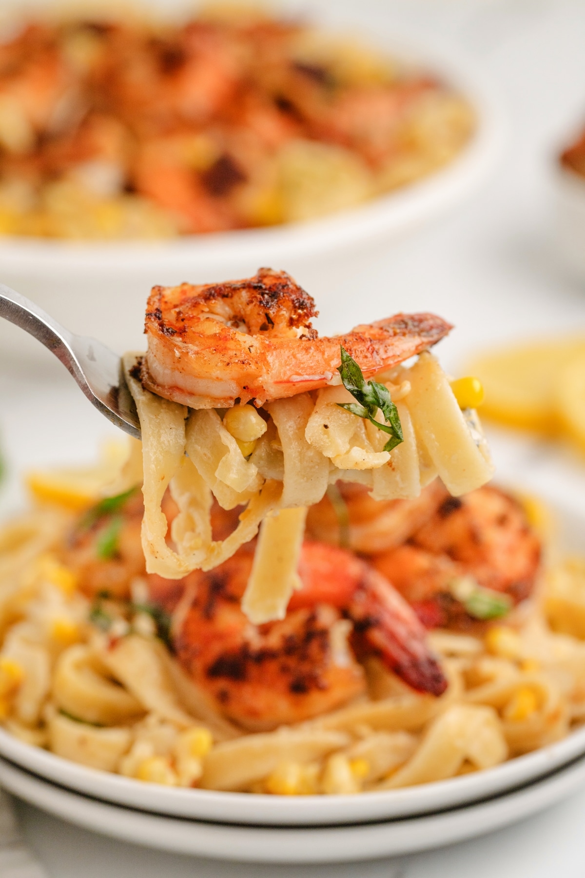 Fork holding a bite of fettuccine with blackened shrimp and charred corn.