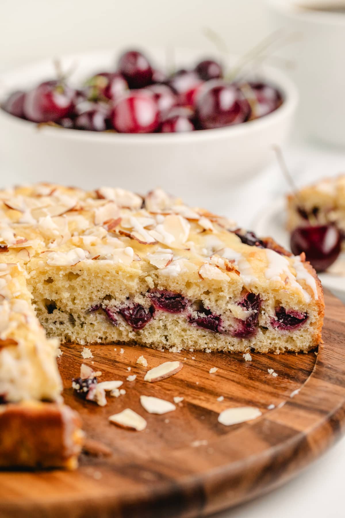 Easy Cherry Almond Coffee Cake with Fresh Cherries Cherry almond coffee cake sliced on a wooden board with fresh cherries in the background