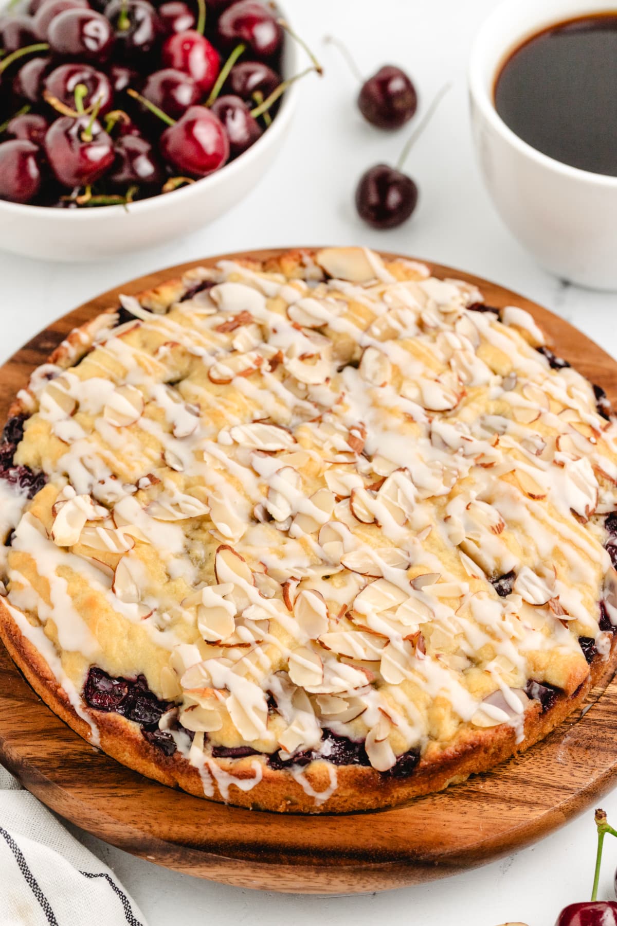 Easy Cherry Almond Coffee Cake with Fresh Cherries Cherry almond coffee cake sliced on a wooden board with fresh cherries in the background