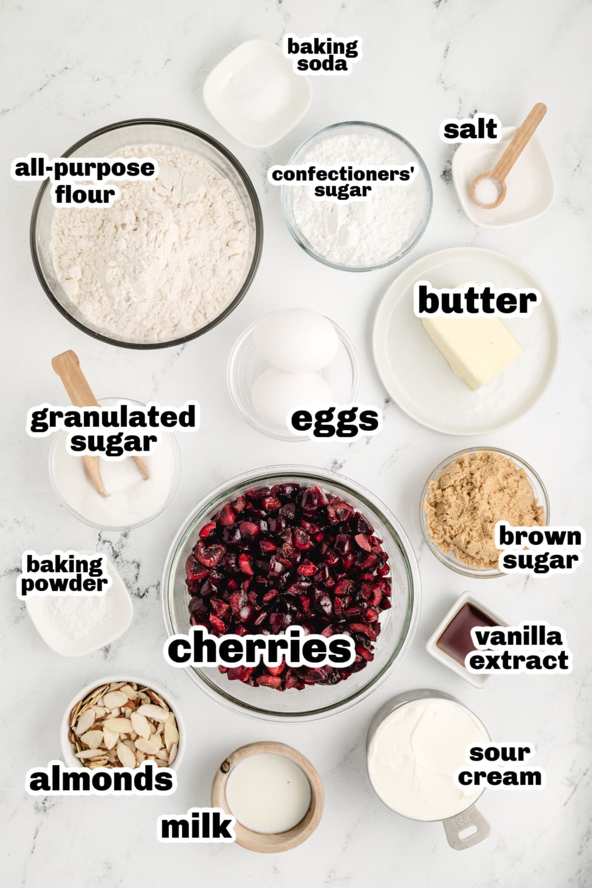 Cherry Almond Coffee Cake Ingredients with Fresh Cherries and Sour Cream Ingredients for cherry almond coffee cake laid out on a white surface, including fresh cherries, sour cream, flour, sugar, almonds, and vanilla