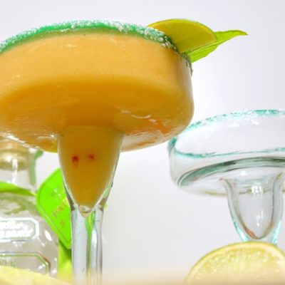 Nectarine margarita in a glass with an empty glass.