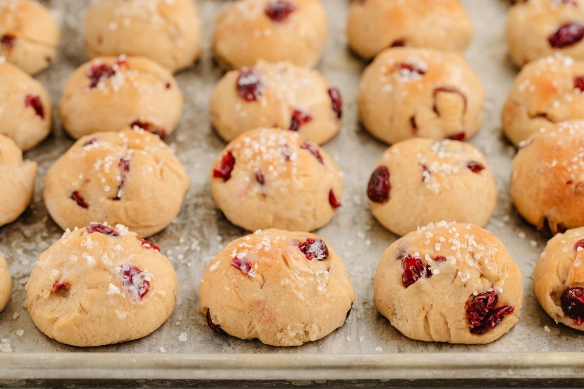 Cinnamon-cranberry dinner rolls on a baking tray. Golden-brown cinnamon-cranberry dinner rolls cooling on a metal baking tray.