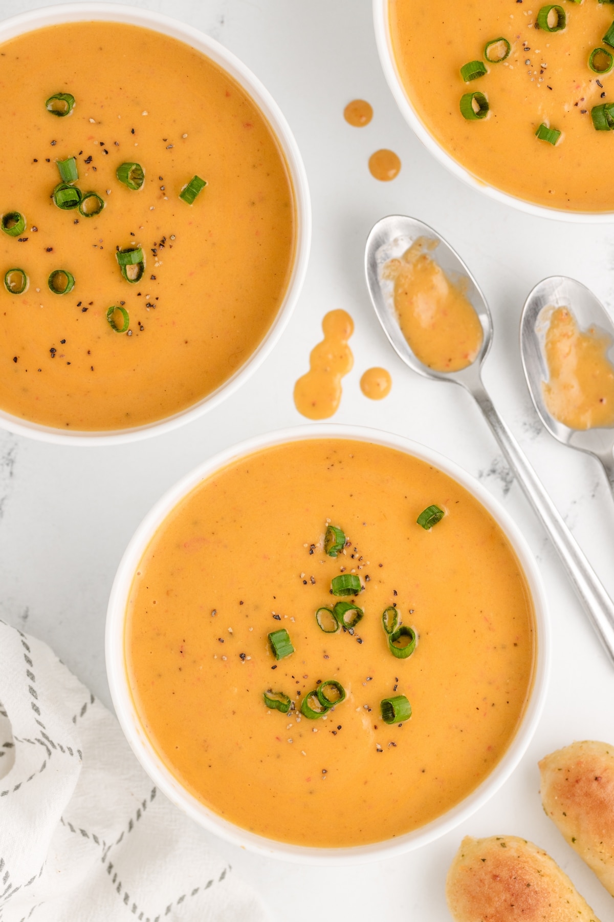 Creamy Red Pepper Coconut Soup in several bowls. Bowl of creamy red pepper coconut soup topped with a drizzle of cream and fresh herbs.