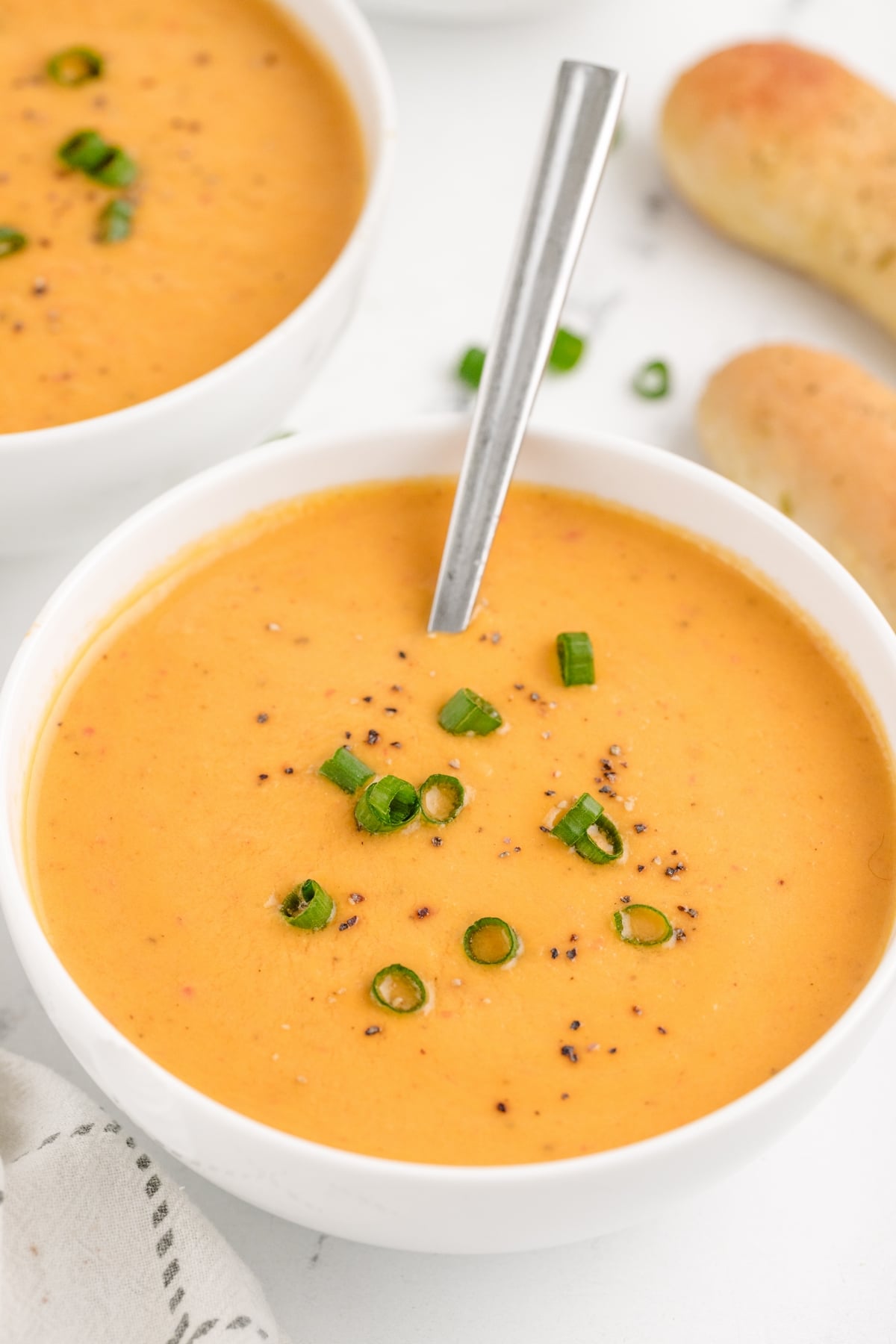 Creamy Red Pepper Coconut Soup with a spoon. Close-up of a creamy coconut soup with red peppers, garnished with a sprinkle of fresh herbs.