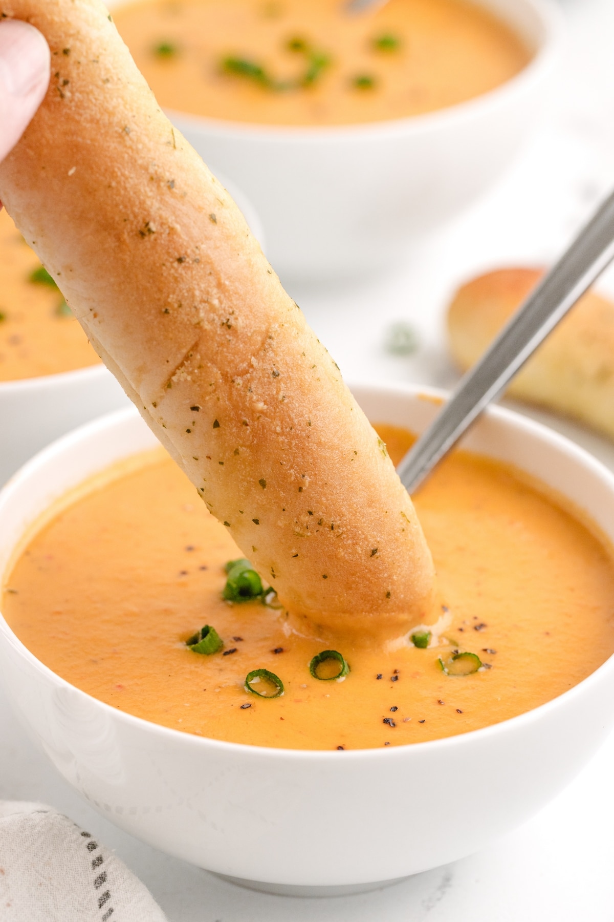 Creamy Red Pepper Coconut Soup with breadsticks. Rich and creamy red pepper coconut soup served with crunchy breadsticks being dipped into a bowl.