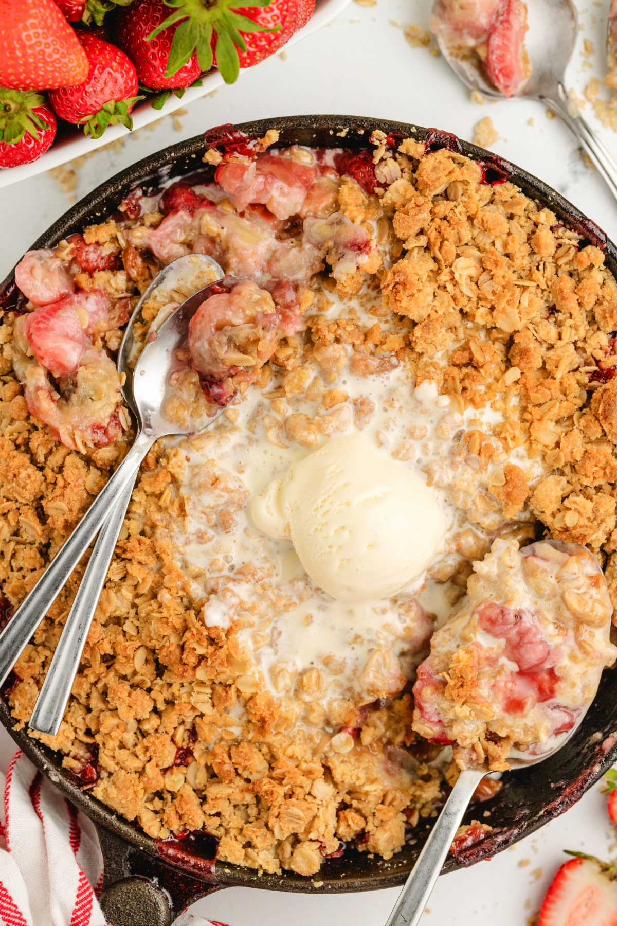 Strawberry banana crumble in skillet with ice cream Skillet strawberry banana crumble served warm with vanilla ice cream and two spoons.