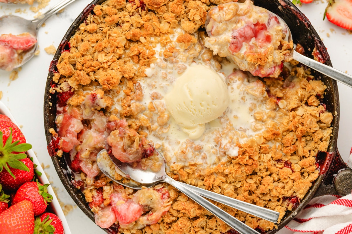 Strawberry banana crisp with oat topping and ice cream Close-up of baked strawberry banana crisp in cast iron skillet with melted vanilla ice cream.