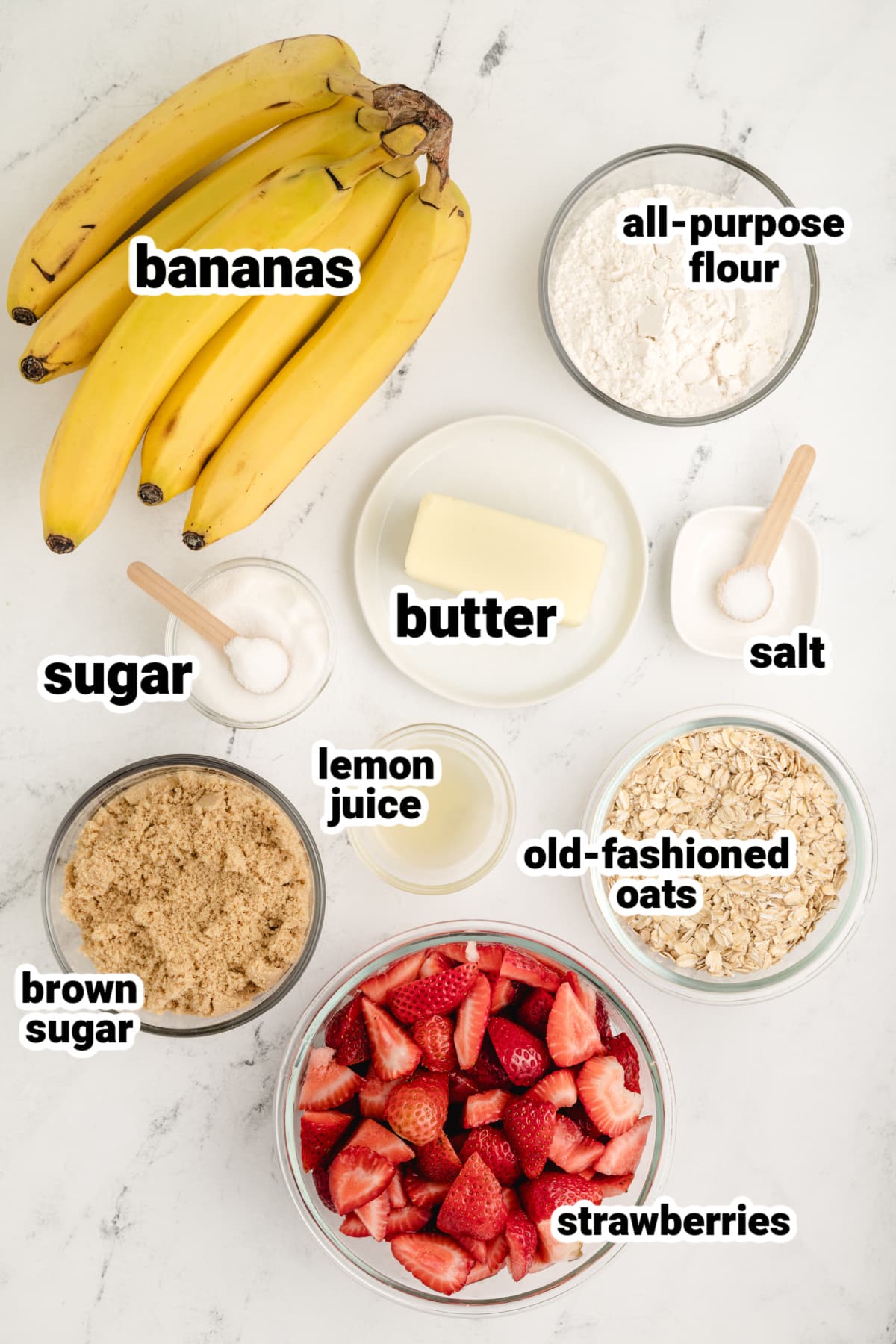 Strawberry banana crumble ingredients on white background All ingredients for strawberry banana crumble laid out: strawberries, bananas, oats, brown sugar, flour, butter.