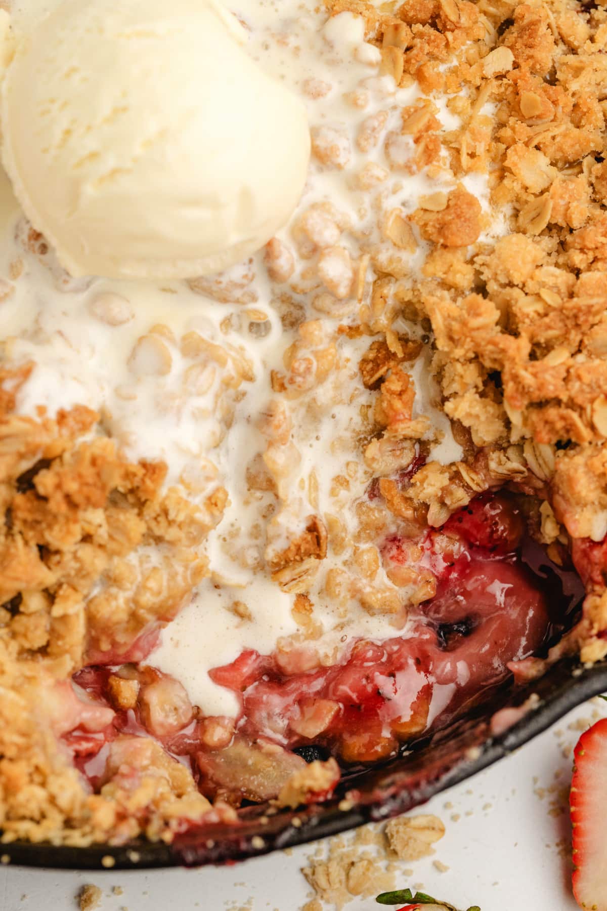 Strawberry banana crumble recipe served warm with ice cream Cast iron skillet of baked strawberry banana crumble with ice cream melting over the top.