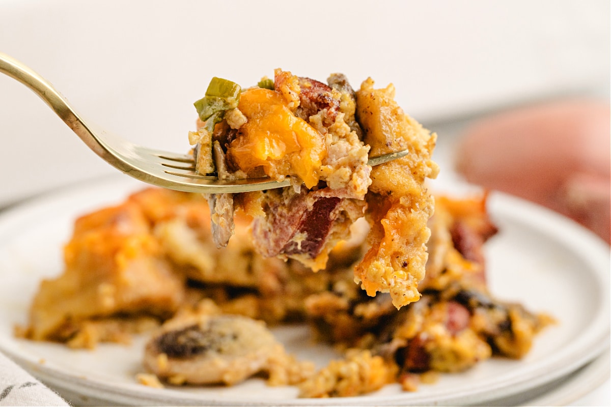Fork lifting a cheesy bite of bagel breakfast casserole with kielbasa.