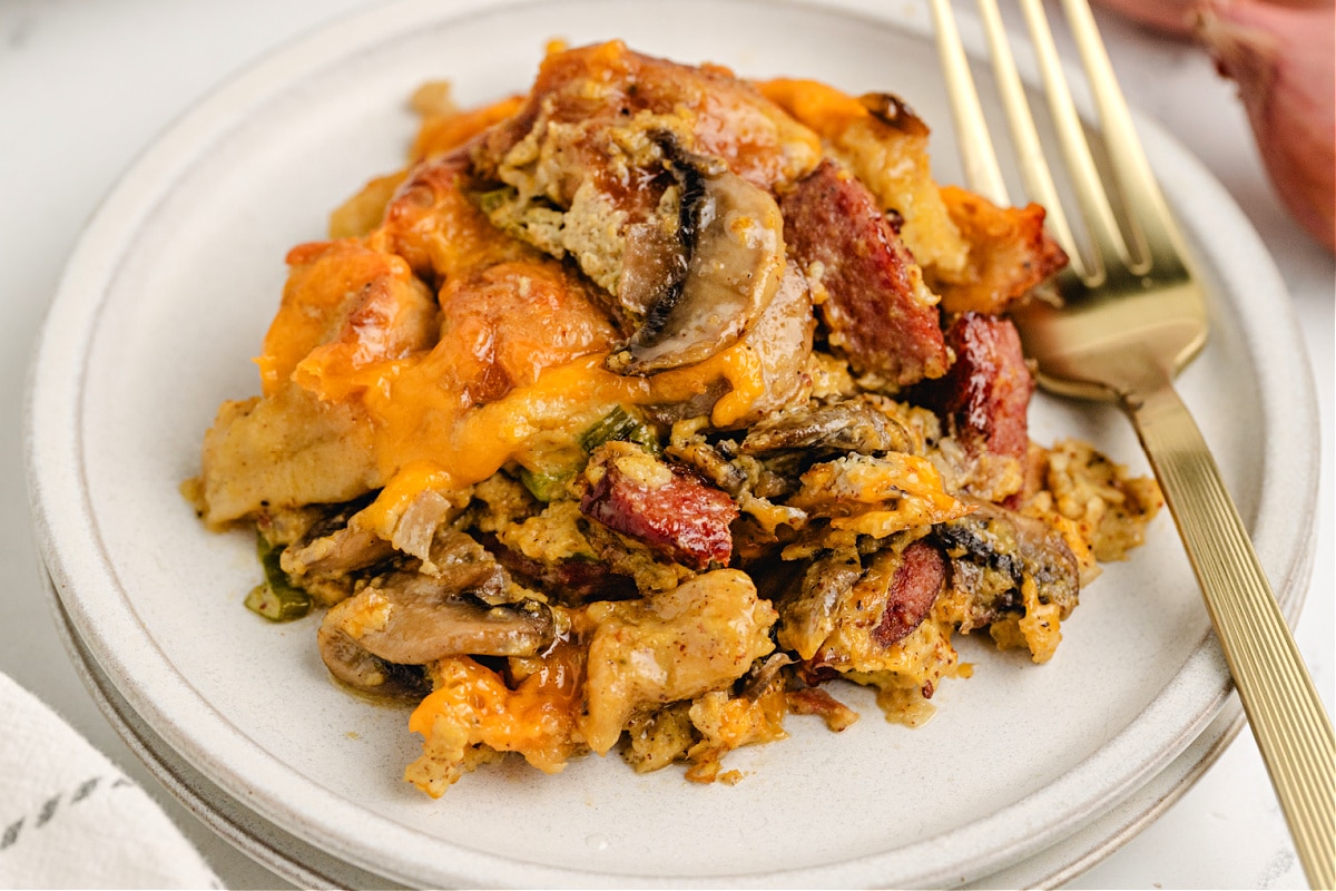 Plate of cheesy egg casserole with kielbasa, mushrooms, and bagel cubes.