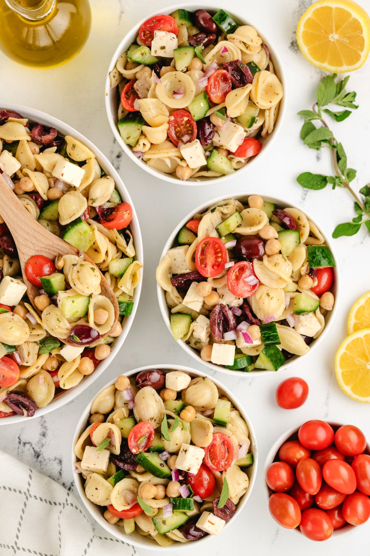 Greek Pasta Salad in several bowls The pasta salad freshly tossed in a large bowl, with dressing evenly coating the pasta and toppings.